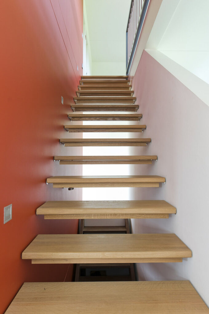 Freitragende Holztreppe vor oranger Wand – Neubau EFH Schneisingen